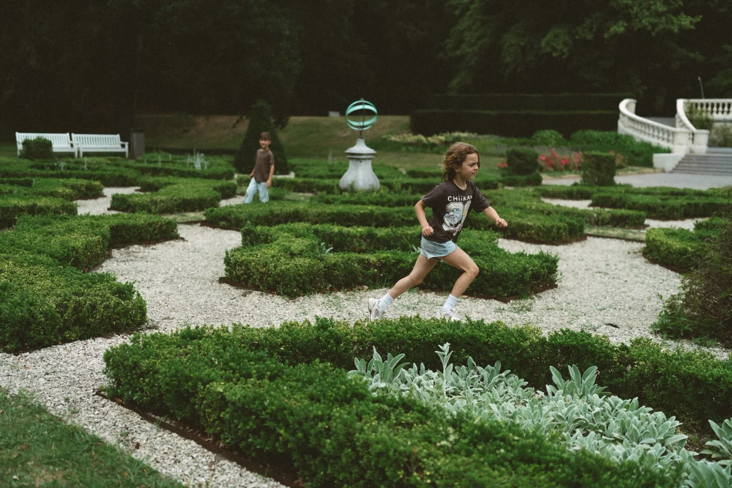 Twee kinderen rennen door een formele tuin met buxushagen