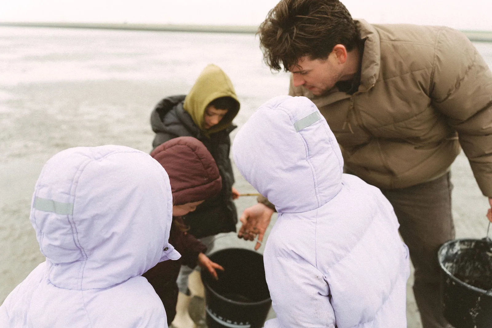 Een vader zoekt met zijn kinderen met emmers naar schelpen op het strand