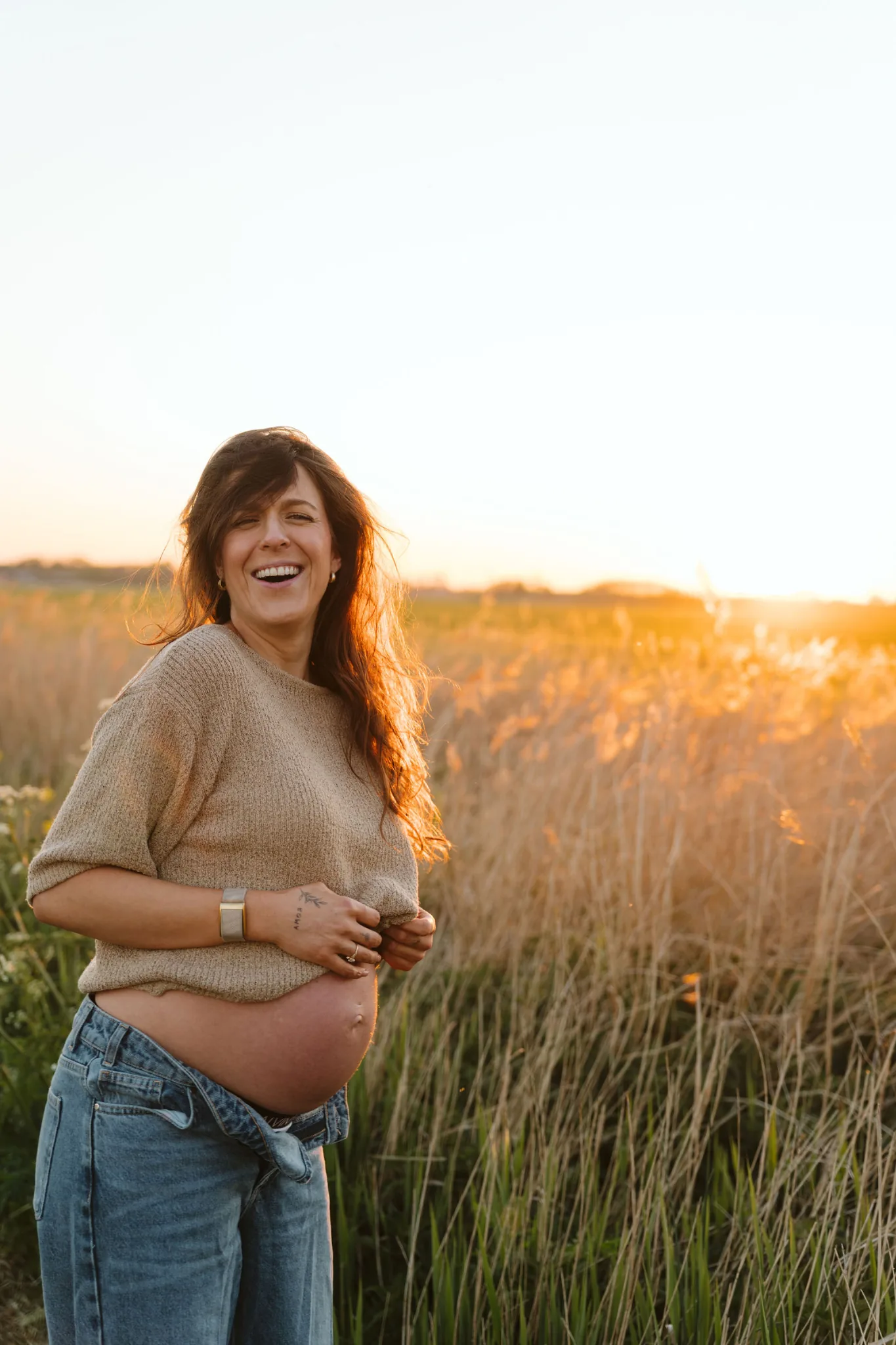 Een zwangere vrouw staat in een veld, de handen om haar buik